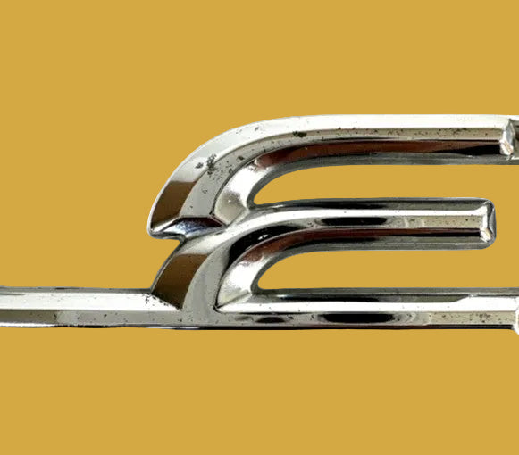 Close-up of a chrome car emblem on a white background